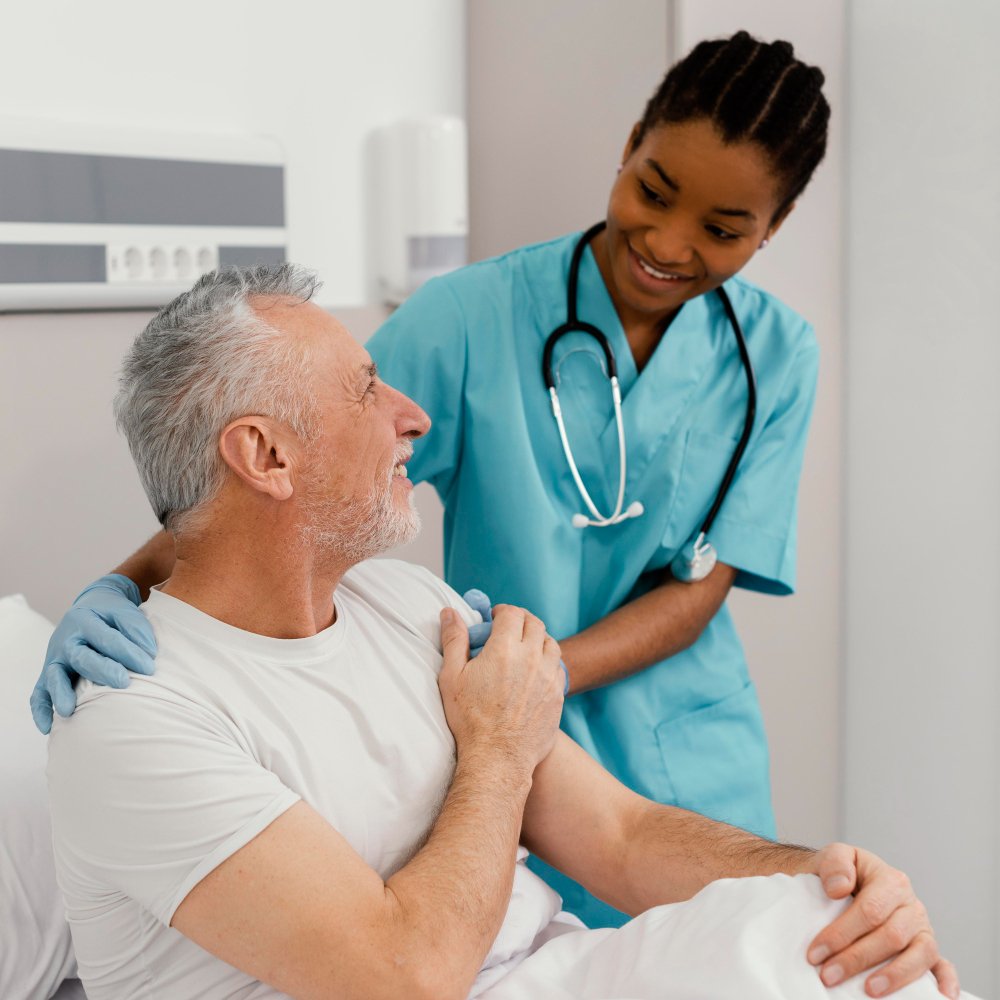 Primary care nurse with a patient Nurse in scrubs speaking with an older patient seated in a hospital bed